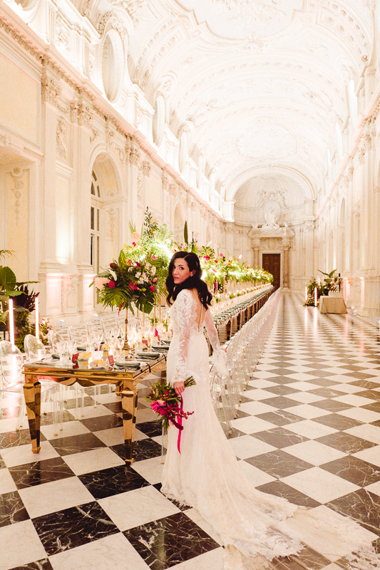 Sposa in primo piano ai piedi di una tavolata imbandita dentro la galleria di Diana di Venaria